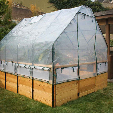 Outdoor Living Today 8×12 Raised Garden Bed stands with its clear plastic cover rolled up slightly to reveal growing plants inside