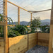 Outdoor Living Today 8×8 Raised Garden Bed is seen from inside, highlighting tall leafy plants growing behind a wooden and wire fence