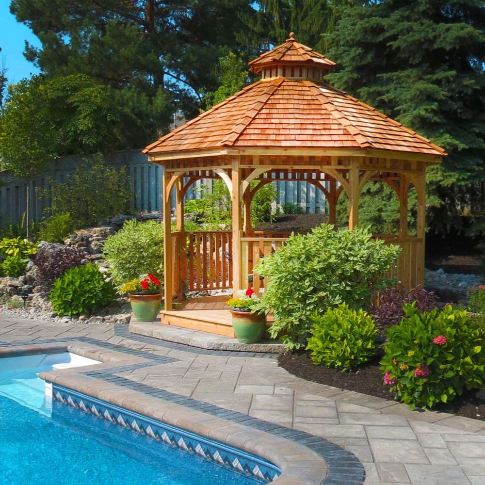 Outdoor Living Today Western Red Cedar Octagon Bayside Gazebo sits beside a pool, surrounded by landscaped plants and stone paving