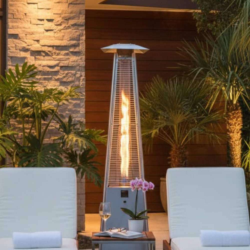 Outdoor Order PrismQuad Tower Heater glows beside a stacked stone wall between two white poolside loungers