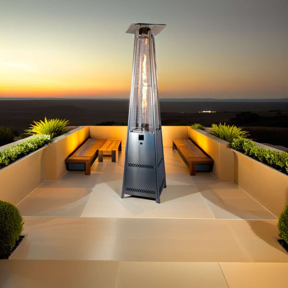 Outdoor Order PrismQuad Tower Heater stands lit at the center of a rooftop terrace with wooden benches at sunset
