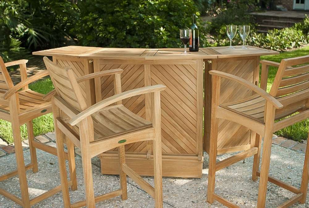 Outdoor patio scene features four stools and a bar table from Westminster Teak Somerset 5pc Teak High Bar Set with wine glasses and a bottle on top