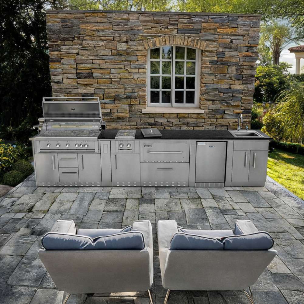 Outdoor setup of Sunstone French Quarter 13ft 7in Outdoor Kitchen Island Package against a stone wall with grill, sink, and fridge