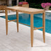 Outdoor teak bar table on a stone patio beside a pool with plants and a fireplace, styled from Westminster Teak Laguna 5pc Teak High Bar Set