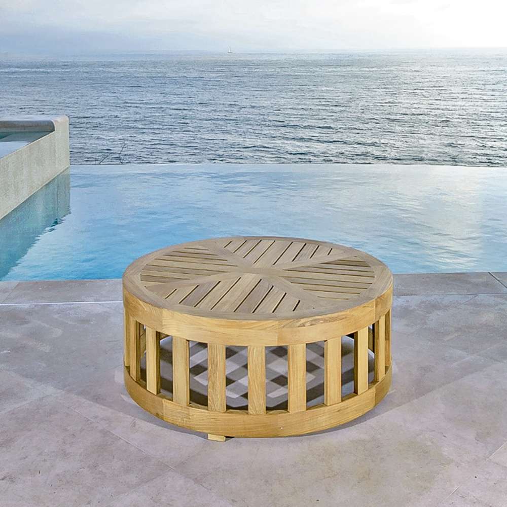 Outdoor view of Westminster Teak 36-Inch Kafelonia Teak Coffee Table on a patio by a pool with an ocean backdrop