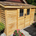 Outdoor Living Today 12×4 with Sliding Doors SpaceSaver Storage Shed is beautifully placed in a garden with blooming flowers surrounding its natural cedar exterior