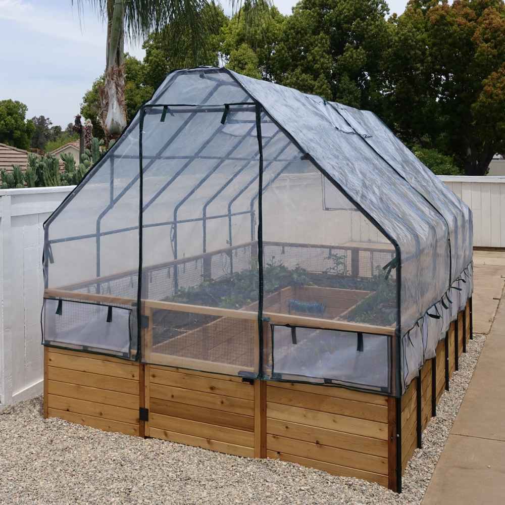 Outdoor Living Today 8×12 Raised Garden Bed sits on a gravel path, fully covered by a translucent greenhouse to shield young crops