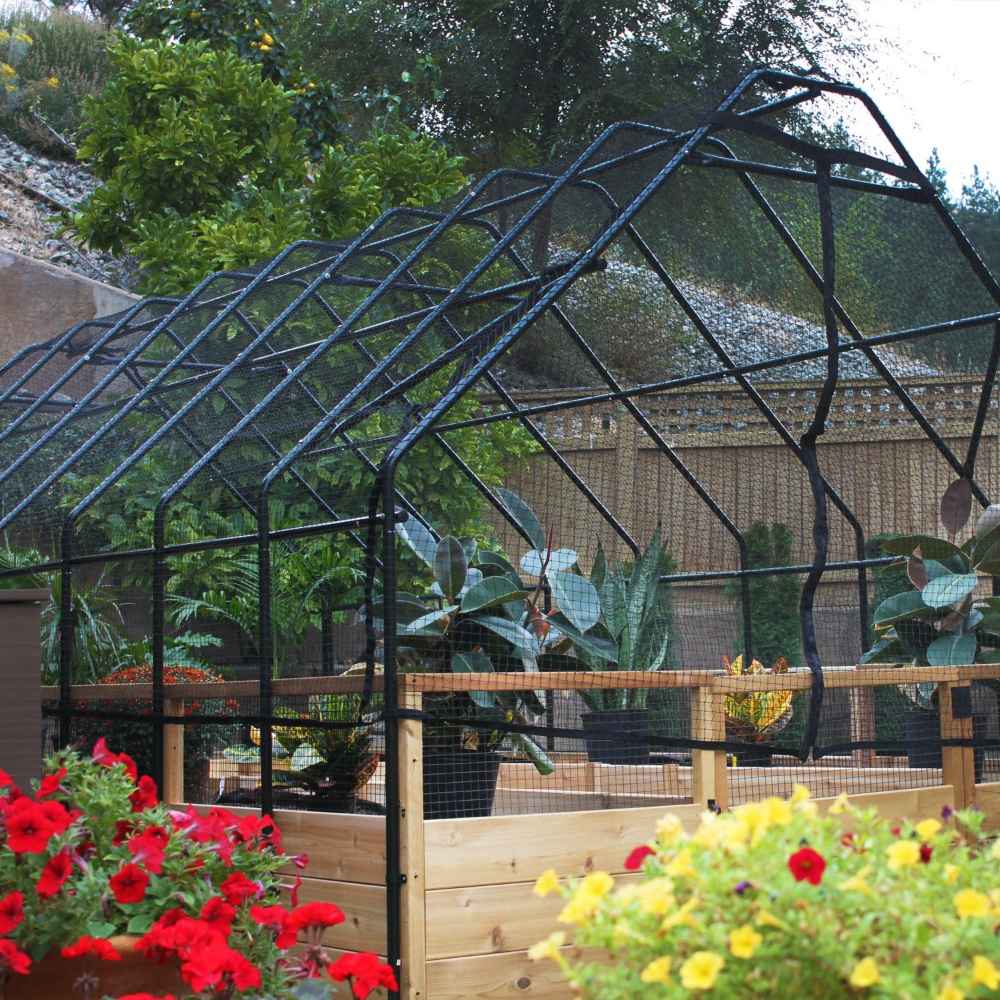 Outdoor Living Today 8×12 Raised Garden Bed stands in a garden surrounded by bright red and yellow flowers, with a black mesh greenhouse cover