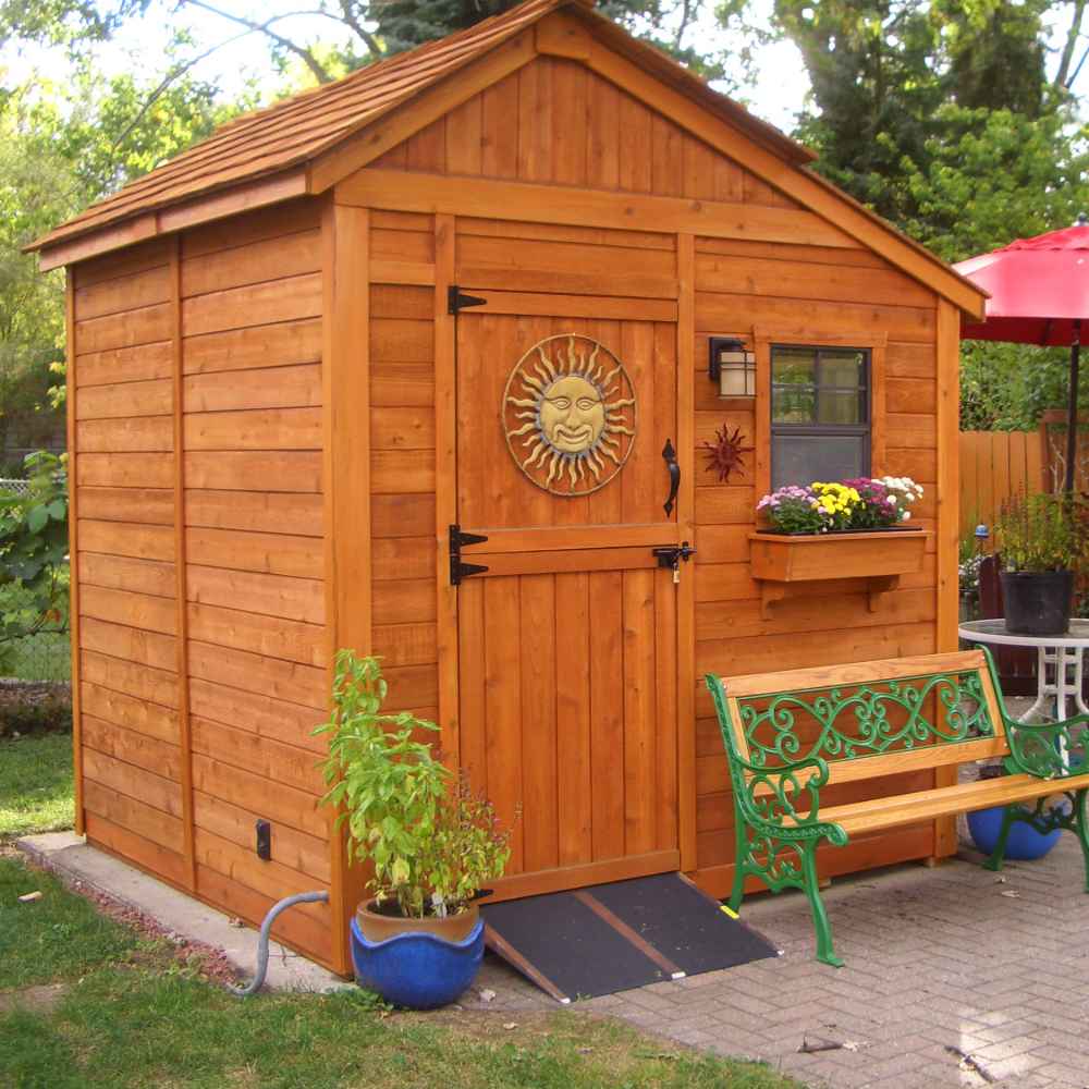 Outdoor Living Today 8×8 Sunshed Garden Shed has a decorative sun emblem on the door, a ramp, and a bench nearby