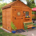 Outdoor Living Today 8×8 Sunshed Garden Shed has a decorative sun emblem on the door, a ramp, and a bench nearby