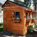 Outdoor Living Today 8×8 Sunshed Garden Shed is placed beside a house with flower-filled boxes, garden lighting, and a green bench in front