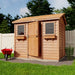 Outdoor Living Today 9×6 Cabana Garden Shed stands in a fenced garden with one door slightly open, cedar roof, and flower boxes beneath its windows