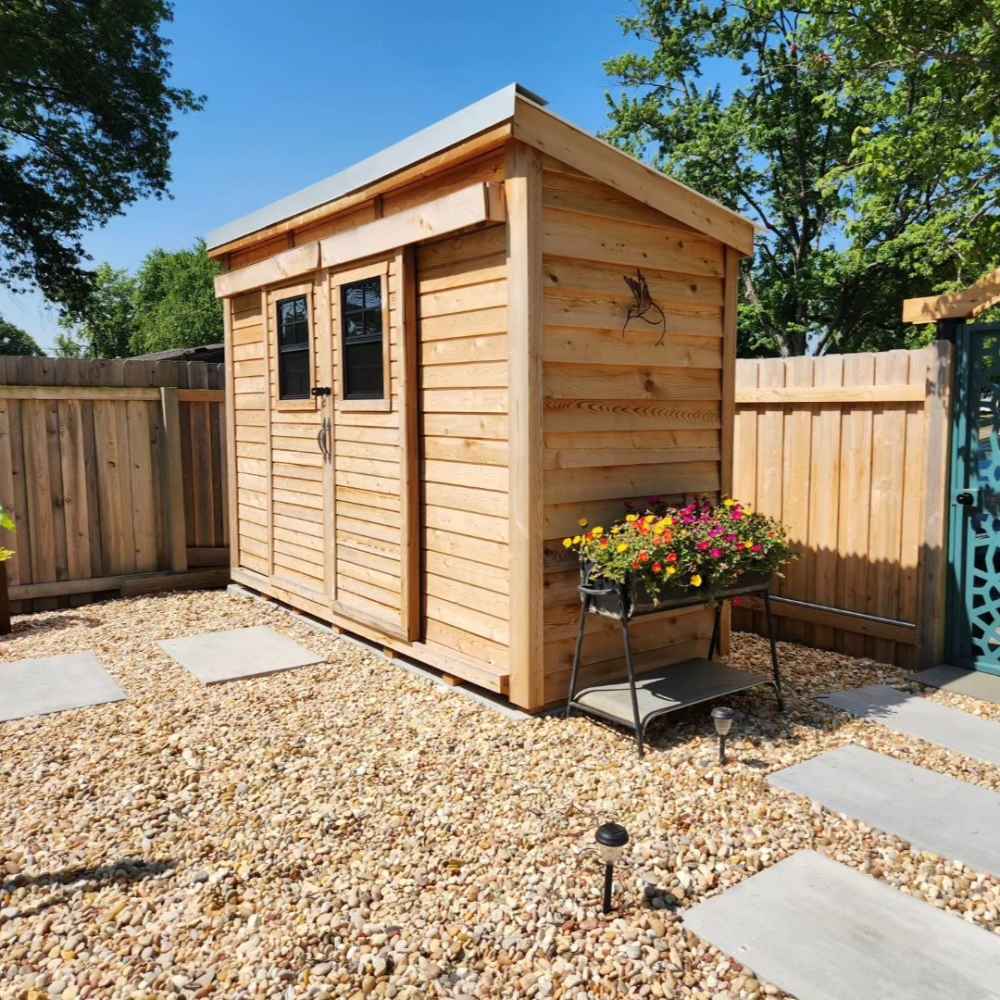 Outdoor Living Today GardenSaver 12×4 with Sliding Doors sits beautifully in a gravel backyard surrounded by flowers and a wooden fence