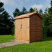 Outdoor Living Today Maximizer 6×6 Wooden Shed stands in a grassy yard, showing its side profile with horizontal wooden panels and a gabled roof