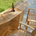 Overhead outdoor view shows the bar table from Westminster Teak Somerset 5pc Teak High Bar Set with a wine bottle and glasses on top beside teak stools