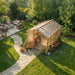 Overhead view shows a stone path leading to the 8x12 Outdoor Living Today Western Red Cedar Greenhouse Kit in a landscaped garden