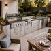 Patio scene featuring the Sunstone French Quarter 13ft 7in Outdoor Kitchen Island Package with grill, prep space, and storage near a dining table