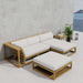 Patio setup of Westminster Teak Maya 4pc Lounge Set with cream cushions, including a sectional sofa, chaise, ottoman, and side table placed beside a wall with a plant and ocean view