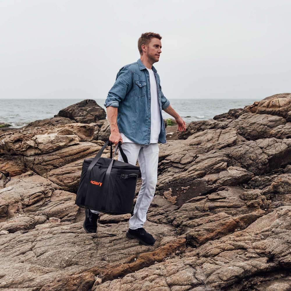 Person carries Jackery Upgraded Carrying Case Bag (L) over rocky ground for easy outdoor transport