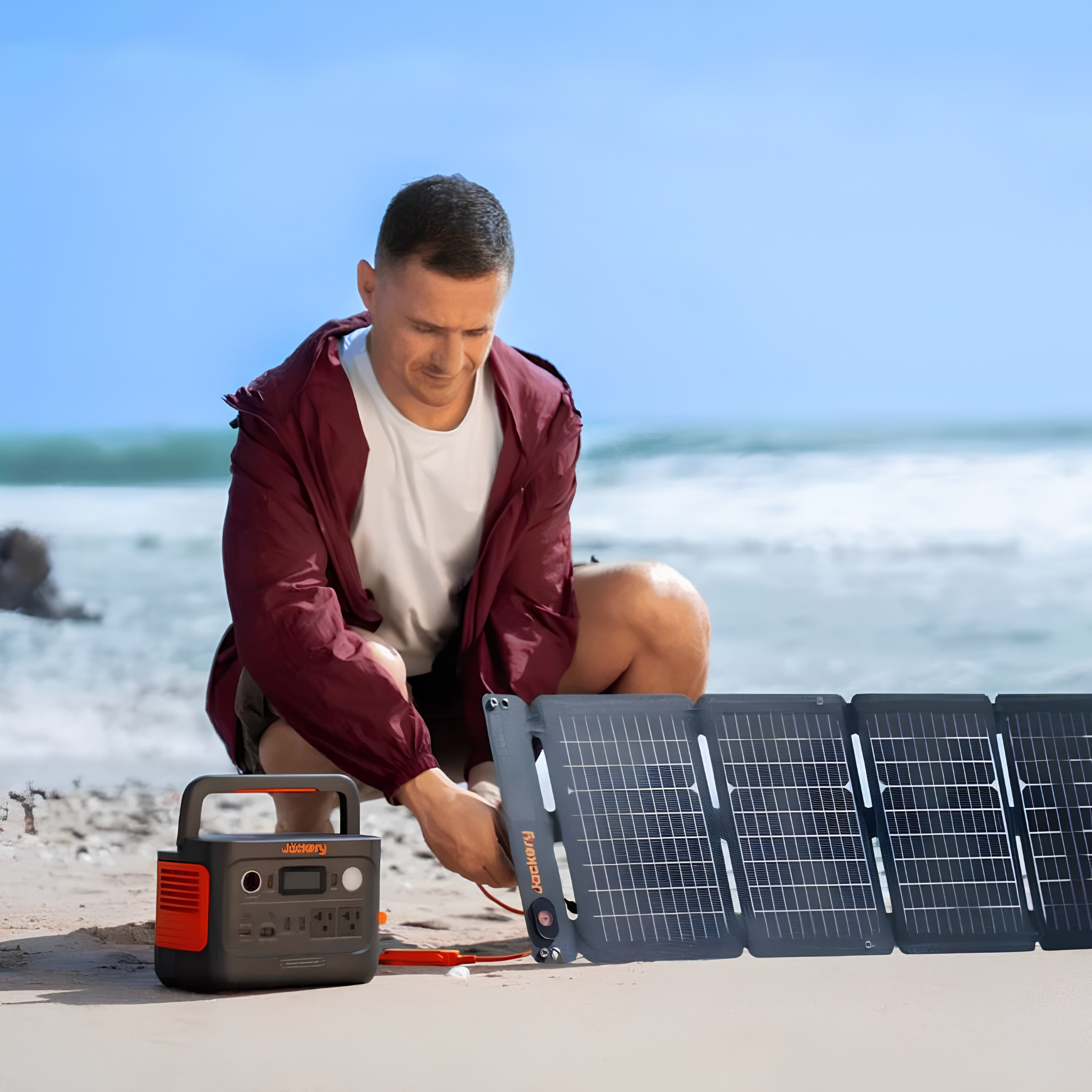 Person connects a foldable solar panel to Jackery Explorer 300 v2 Portable Power Station on a sandy beach for solar charging