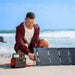 Person connects a foldable solar panel to Jackery Explorer 300 v2 Portable Power Station on a sandy beach for solar charging