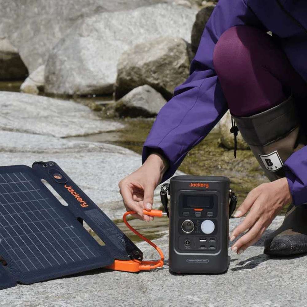 Person connects a foldable solar panel to Jackery Explorer 300D Portable Power Station beside a rocky stream