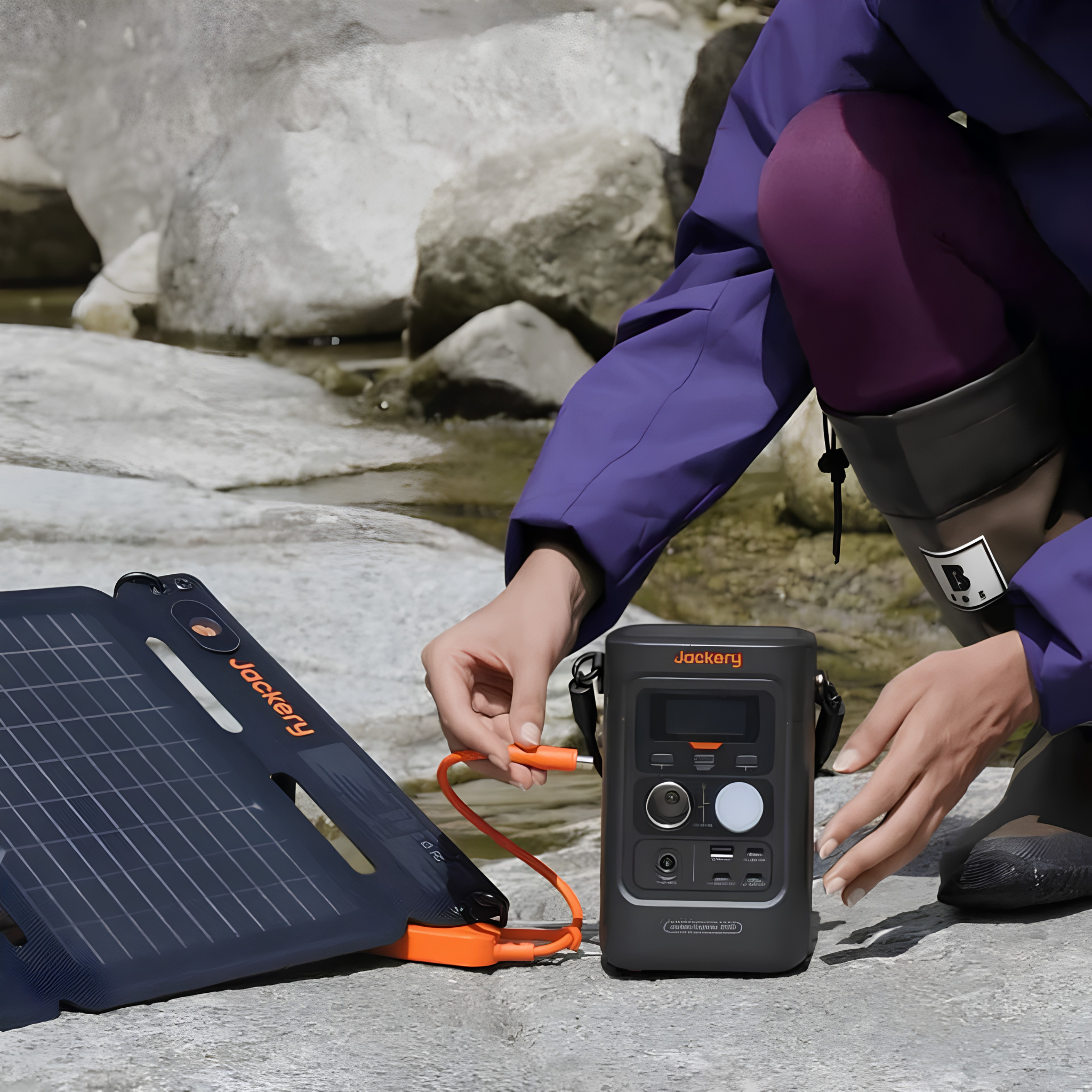 Person connects a foldable solar panel to Jackery Explorer 300D Portable Power Station beside a rocky stream