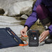 Person connects a foldable solar panel to Jackery Explorer 300D Portable Power Station beside a rocky stream