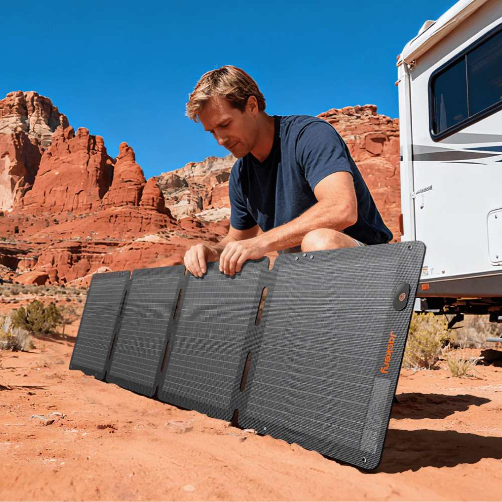 Person unfolds Jackery SolarSaga 100W Air Solar Panel beside an RV in a desert campsite