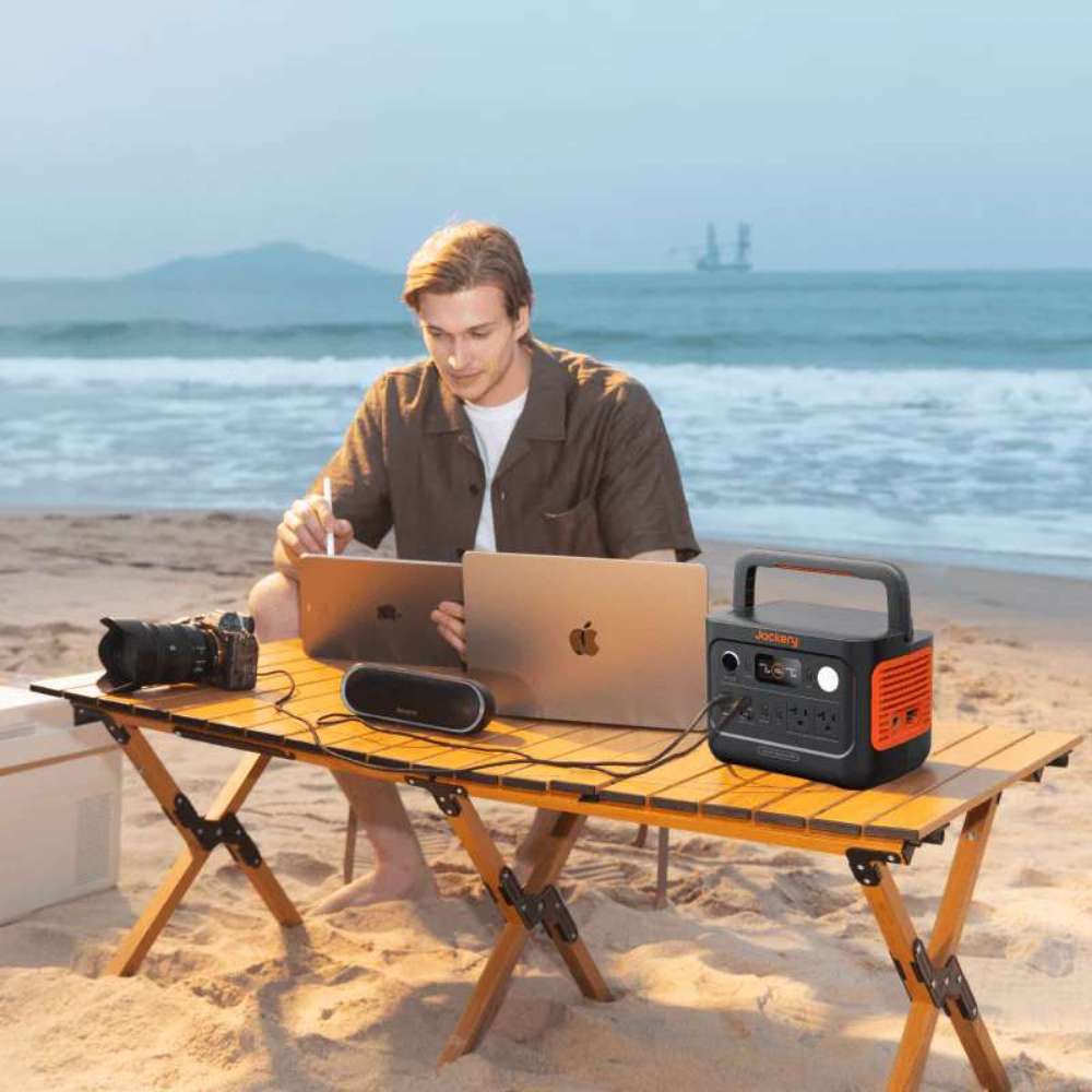 Person works on laptops at the beach while Jackery Explorer 300 v2 Portable Power Station powers devices from a portable table