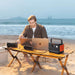 Person works on laptops at the beach while Jackery Explorer 300 v2 Portable Power Station powers devices from a portable table