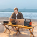 Person works on laptops at the beach while Jackery Explorer 300 v2 Portable Power Station powers devices from a portable table
