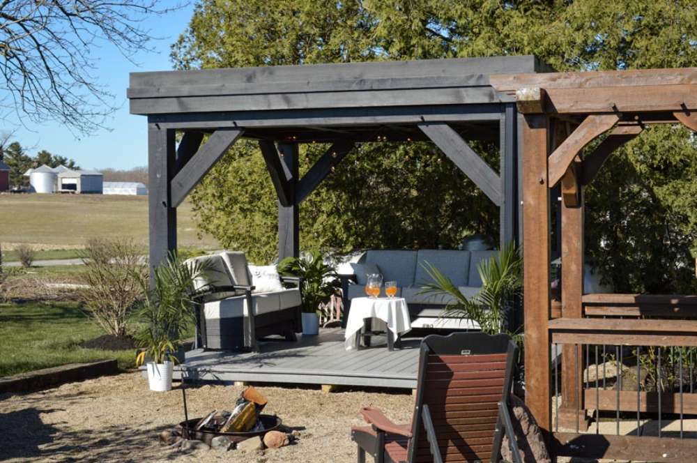 Positioned next to a rustic wooden deck, the Brookside Timber Frame Zion Resort Pergola blends seamlessly with outdoor furniture and natural elements