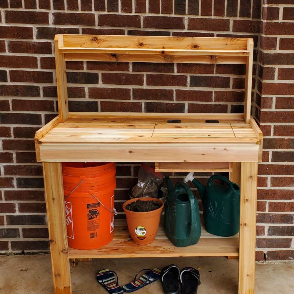 Potting bench against a brick wall holds tools and supplies, with Outdoor Living Today 4×2 Western Red Cedar Potting Bench at the center