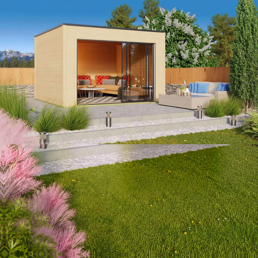 A landscaped backyard scene features the GardenHouse24 USA Q Bic ALU 44A Garden Room furnished with cozy seating and surrounded by greenery and a mountain backdrop