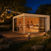 Q Bic ALU 70F Sauna during a bright summer evening with three adults relaxing inside and warm garden lights outside.