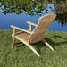 Rear view of Westminster Teak Adirondack Lounger and Ottoman on a grassy lakeside, highlighting its curved teak frame, wide armrests, and slatted back