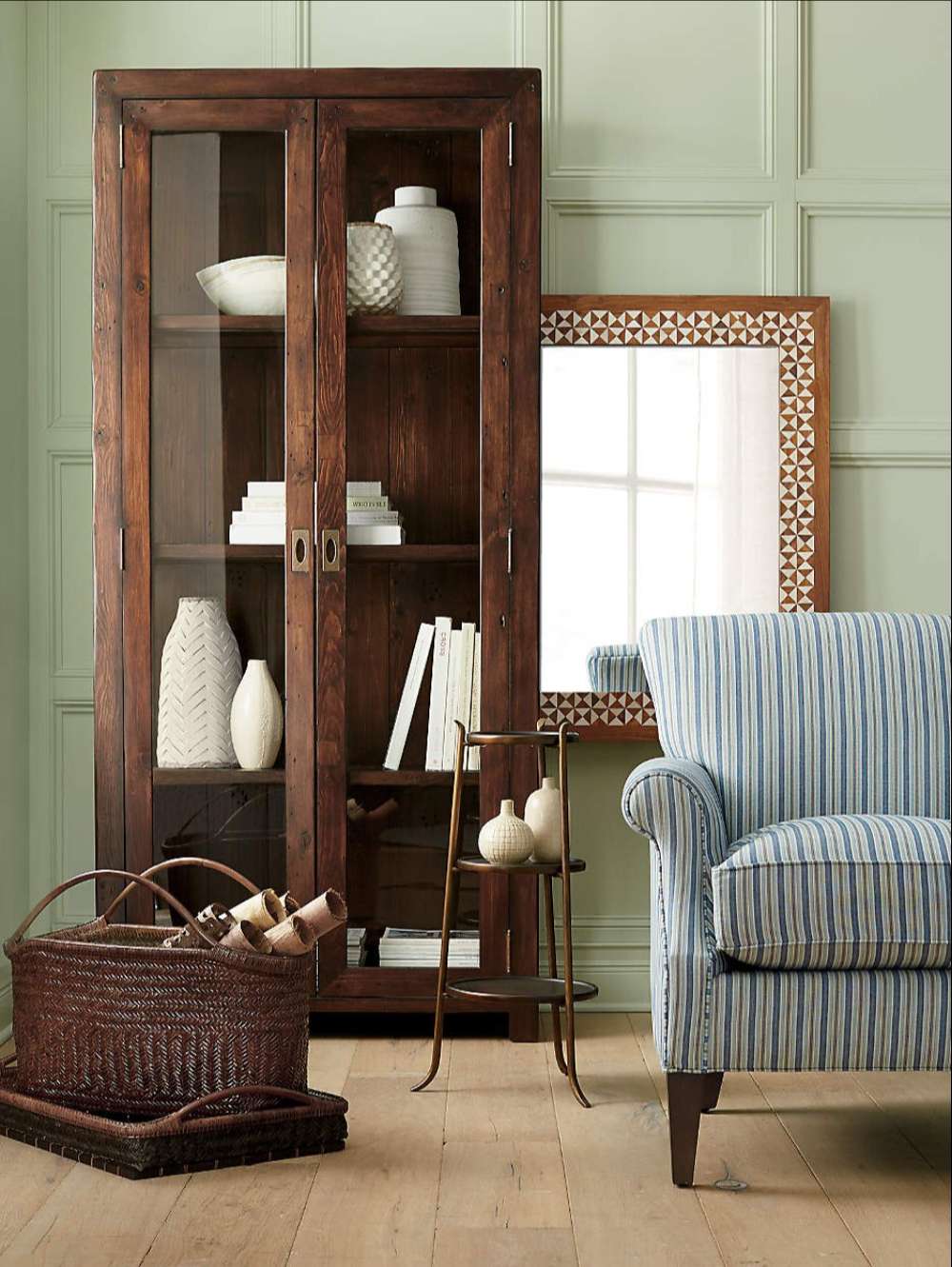 Rustic Crate & Barrel Morris 36" Chocolate Brown Wood and Glass Bookcase Cabinet styled with décor beside a striped armchair