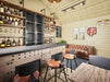 Sawmill Structures BlueWater Bungalow 160 Garden Room showcases a rustic bar counter, leather couch, and open shelving stocked with liquor bottles