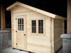 Sawmill Structures Bluewater Den 67 Garden Room, a small wooden cabin with a front door and twin-paned windows under a slanted roof