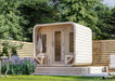 Sawmill Structures Box Sauna from a side angle surrounded by flowers and trees