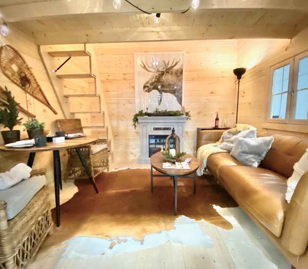 Sawmill Structures Grand Loft 107 Deluxe DD Garden Room’s main floor includes a cowhide rug, a small dining area, and stairs leading up past the fireplace and sofa