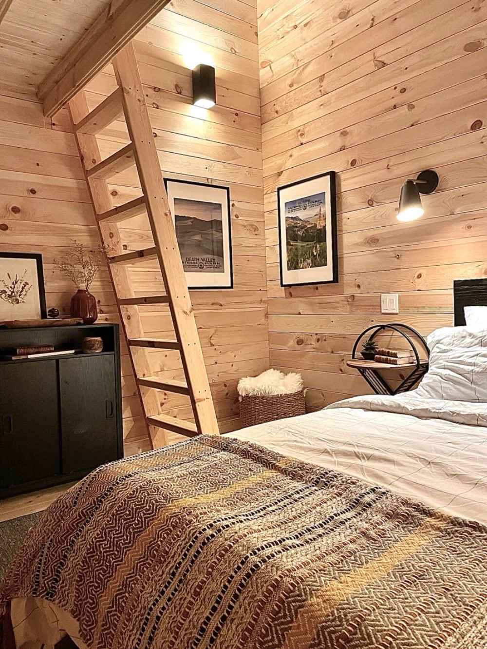 Sawmill Structures Ontario Grand Loft 107 SD Garden Room includes a main floor bedroom with a rustic ladder leading to the loft and framed art on pine walls