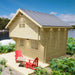 Sawmill Structures Ontario Grand Loft 107 SD Garden Room is a charming two-story wood cabin with a patio and red chairs by the lake
