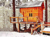Sawmill Structures The Jumbo Grand Loft 130 SD Garden Room sits elevated on a snowy forest deck, its warm wooden exterior glowing against the winter landscape