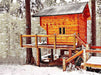 Sawmill Structures The Jumbo Grand Loft 130 SD Garden Room sits elevated on a snowy forest deck, its warm wooden exterior glowing against the winter landscape