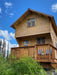 Sawmill Structures The Jumbo Grand Loft 130 SD Garden Room stands tall with a balcony and upper loft window surrounded by lush green landscape and blue skies
