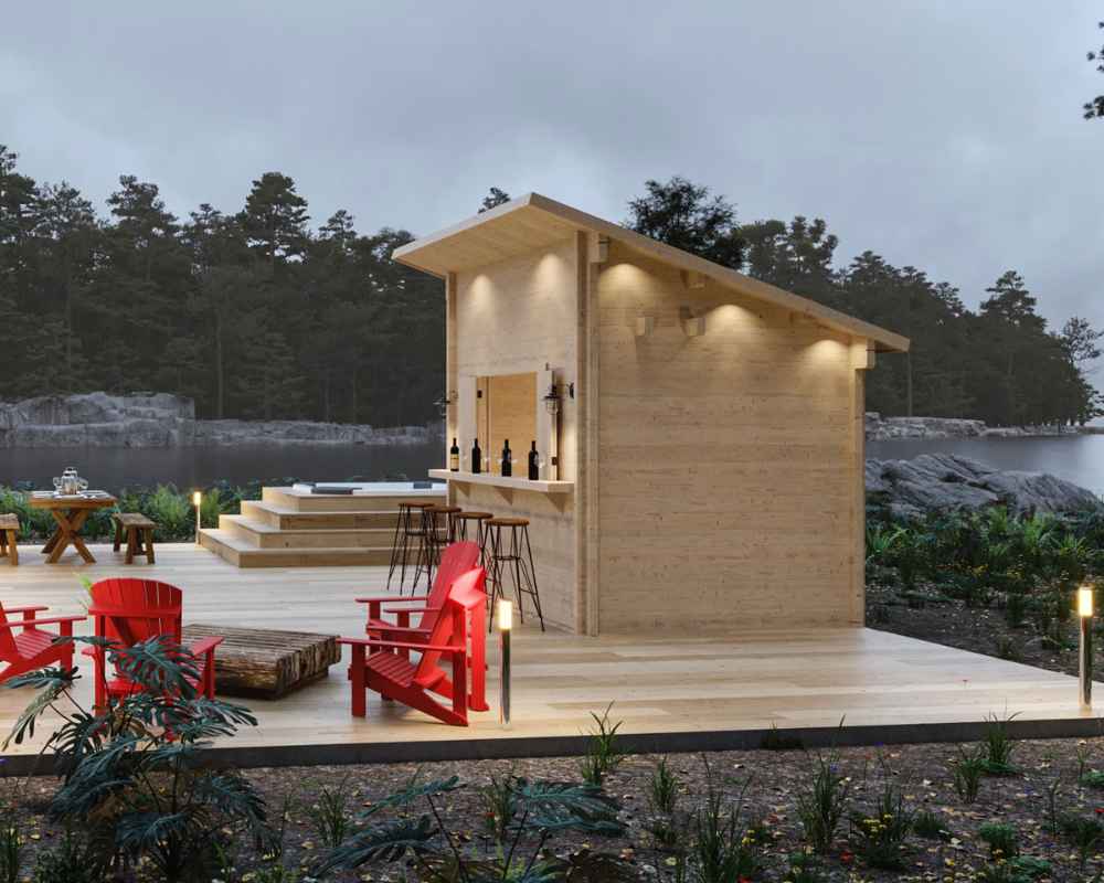 Sawmill Structures The Lakeside Versa Cabana 67 Garden Room stands on a lakeside deck at dusk, beautifully lit with warm lights and surrounded by Adirondack chairs and nature