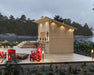 Sawmill Structures The Lakeside Versa Cabana 67 Garden Room stands on a lakeside deck at dusk, beautifully lit with warm lights and surrounded by Adirondack chairs and nature