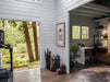 Sawmill Structures The Versa 240 70MM Garden Room opens to a home office with a desk, shelving, plants, and an adjacent fitness area